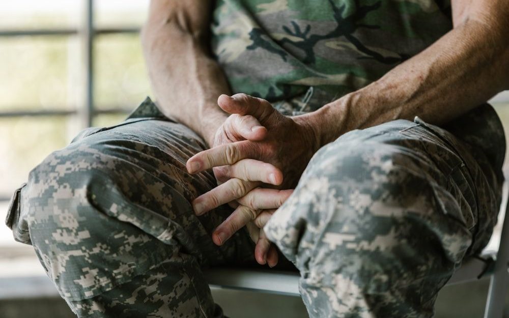 Person in a camouflage uniform seated with hands clasped