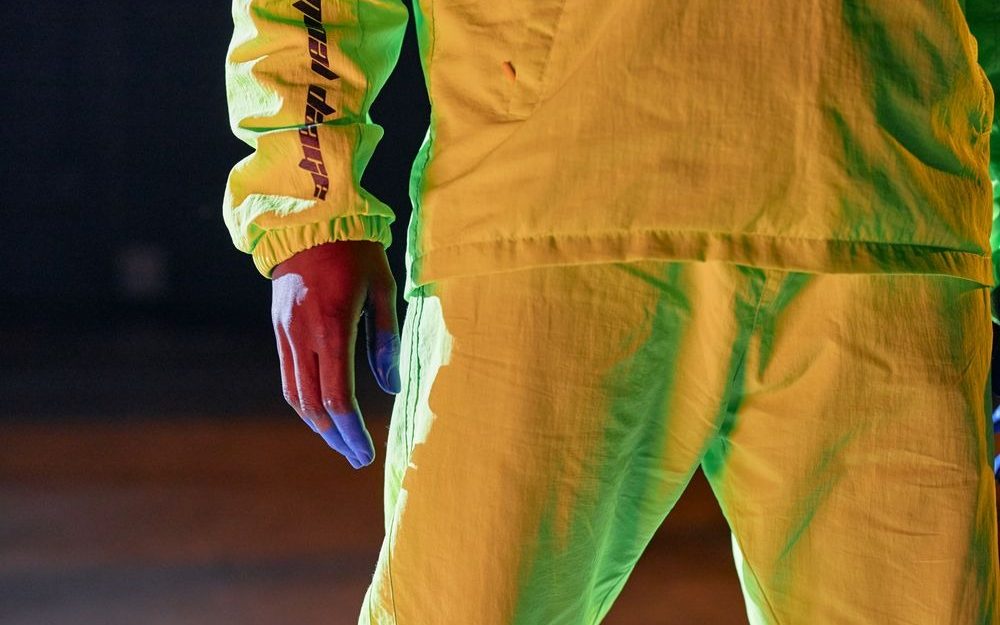 Person in a neon-yellow jacket and trousers lit by coloured light